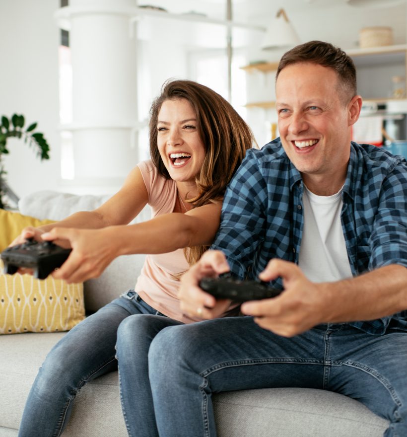 Husband and wife playing video game with joysticks in living room. Loving couple are playing video games at home.